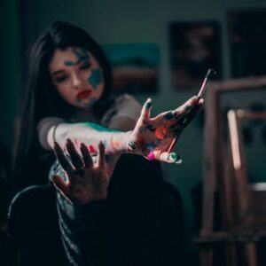 Young woman artist showing creativity with colorful paint on hands in the studio.